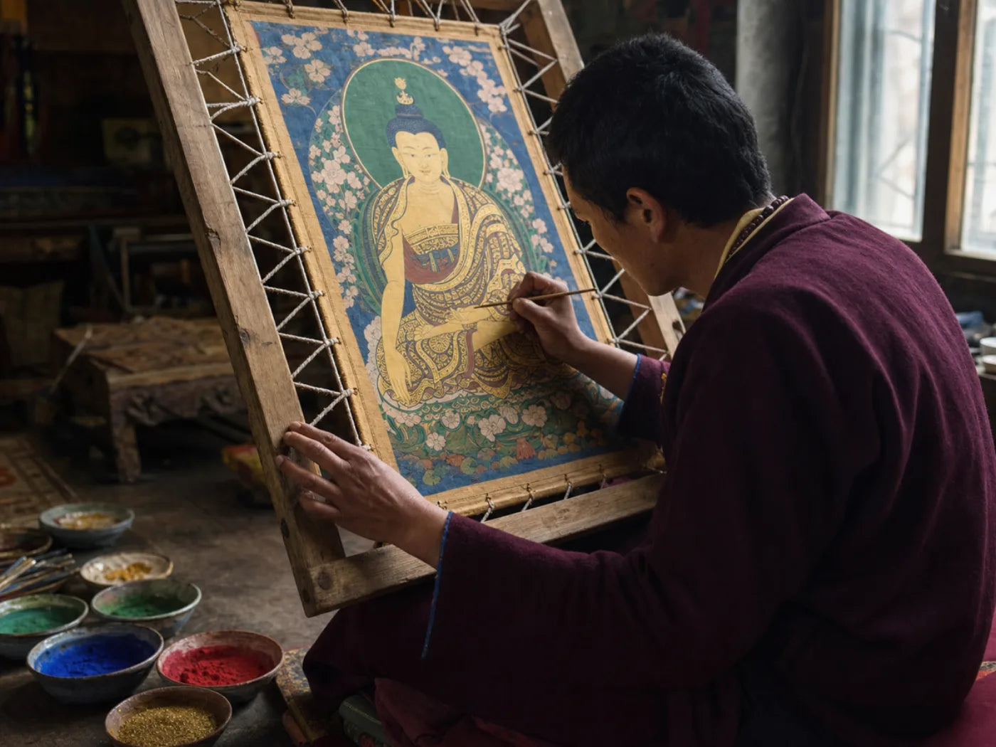 A painter in Regong at work on a thangka held upright in its wooden stretcher